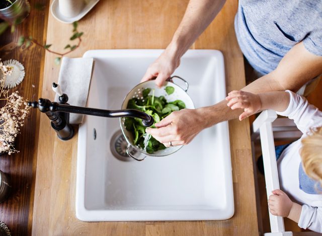 woman pouring water in kitchen sink over lettuce