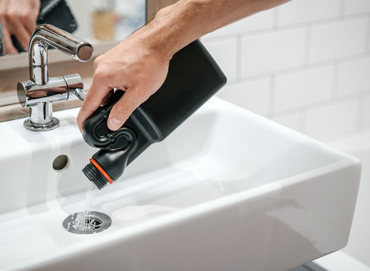 hand pouring drain cleaner into sink drain
