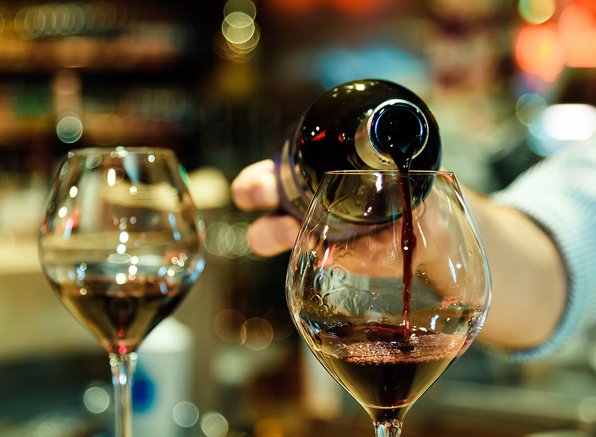 person pouring red wine into two glasses