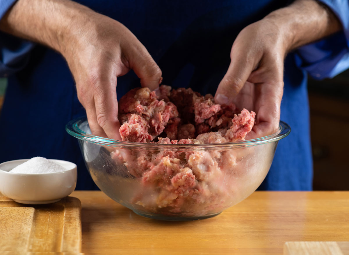Season ground beef mixing with hands in glass bowl