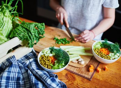 Woman chopping up vegetables to make plant based vegetarian bowl