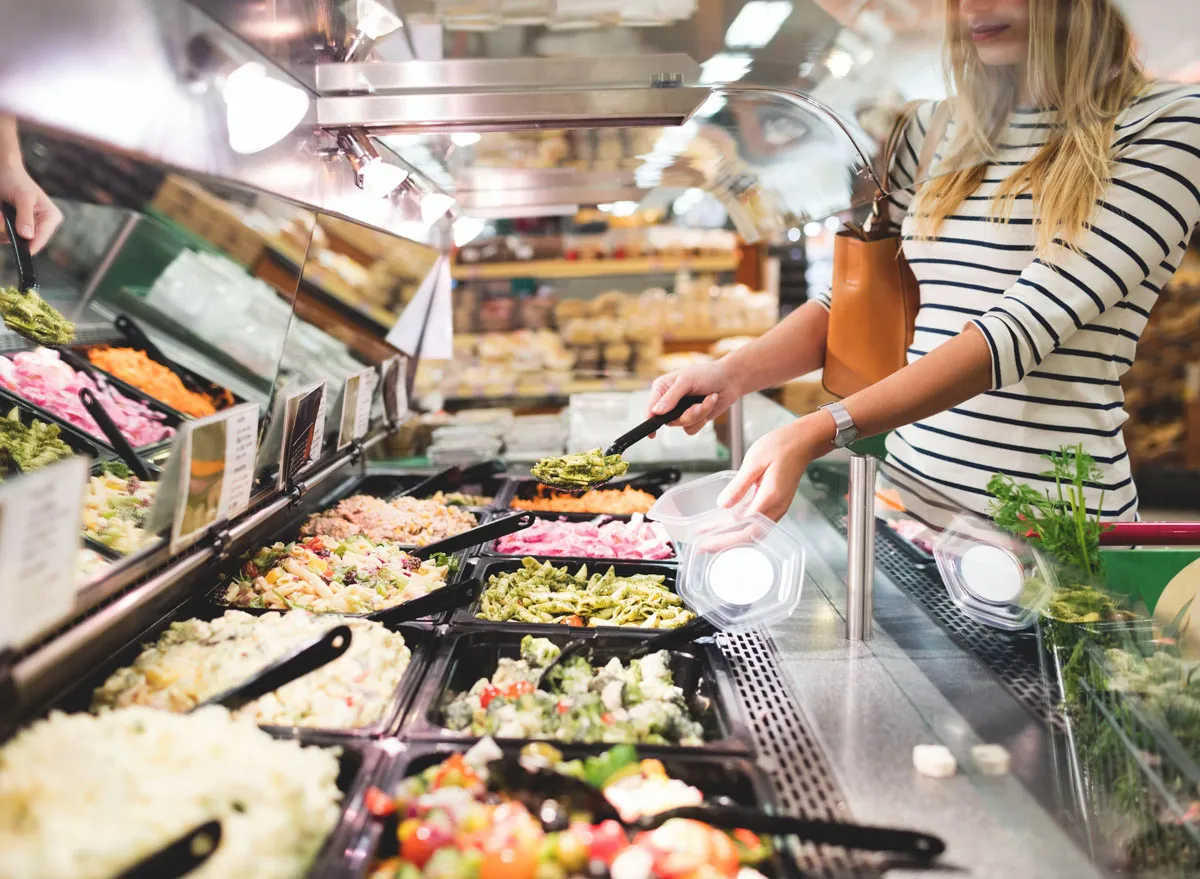 Woman at grocery store serving prepared food at salad bar