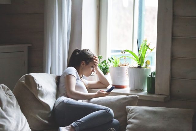 Woman sitting on bed looking at phone bored and in a bad mood