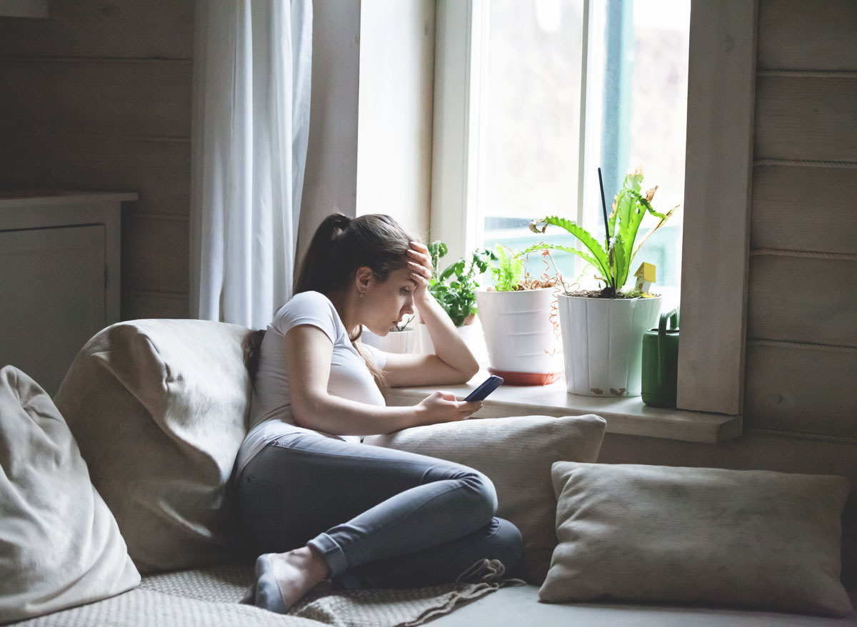 Woman sitting on the bed looking at the phone bored and in a bad mood