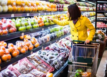 woman wearing a yellow coat scans the produce section of a grocery store