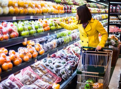 woman wearing a yellow coat scans the produce section of a grocery store