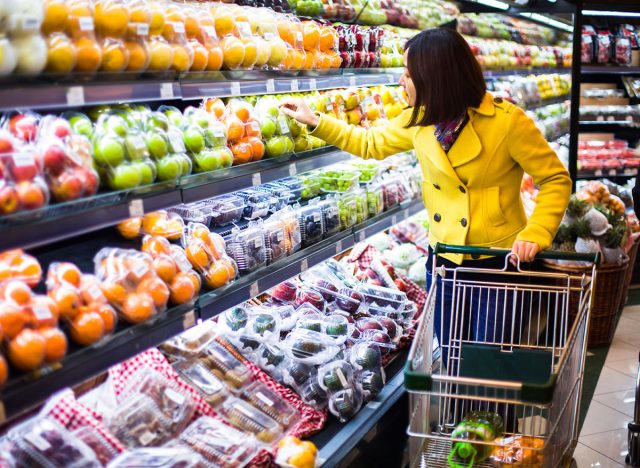 woman wearing a yellow coat scans the produce section of a grocery store