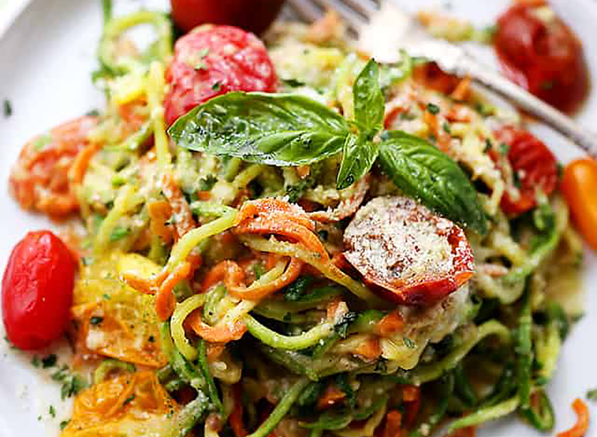 carrot zucchini noddles with tomatoes and parmesan tossed together on a plate and sprinkled with basil