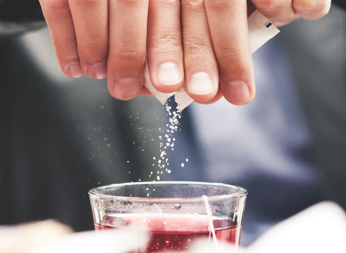 Man pouring added sugar packet into drink