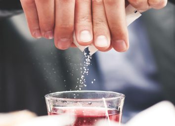 Man pouring added sugar packet into drink