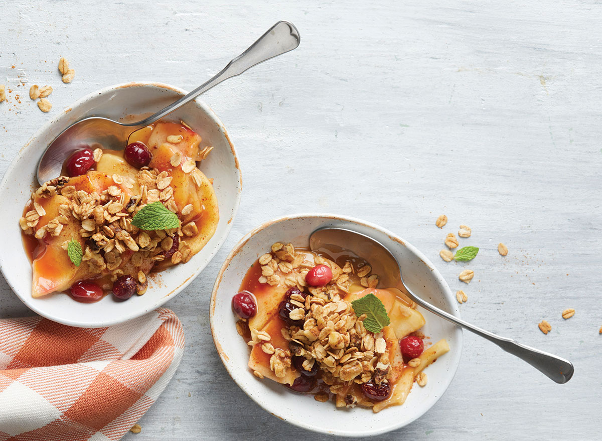 apple cranberry crisp in while bowls with spoons and red gingham napkin on wooden background