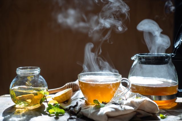 Hot tea in glass teapot and cup with steam on wood background