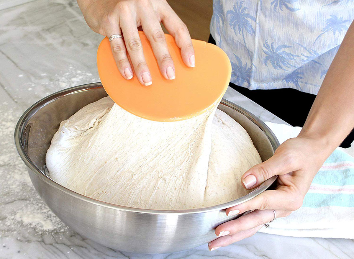 person mixing bowl of bread dough with orange bowl scraper
