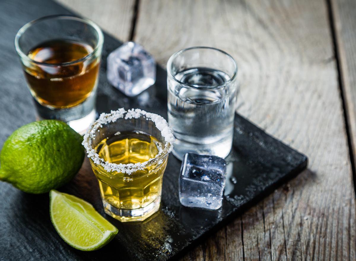 three shots of different liquors with ice cubes and lime