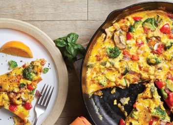 loaded vegetable frittata in cast iron skillet with slice on plate and fork