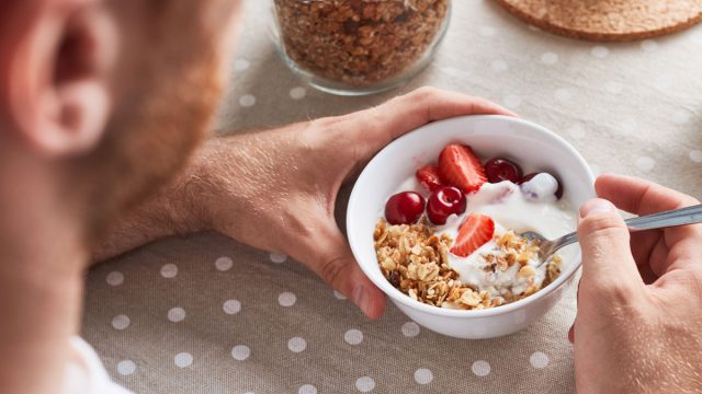 Man scooping into yogurt fruit granola breakfast bowl