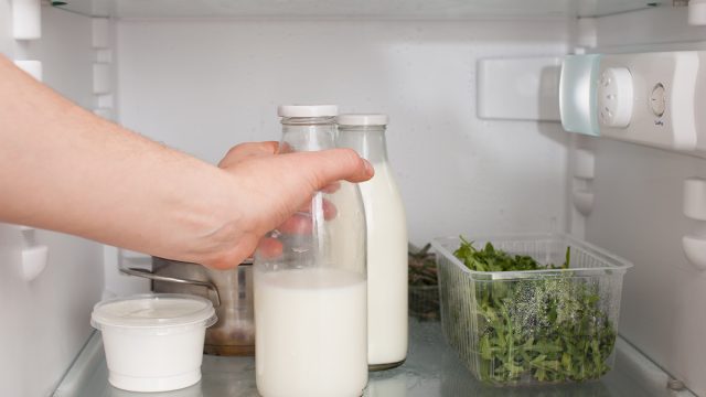 person putting a glass jar of milk in the refrigerator