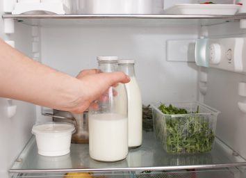 person putting a glass jar of milk in the refrigerator