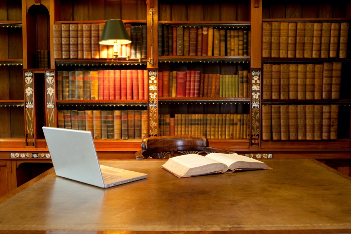 Laptop and book lying on a desk in classic library
