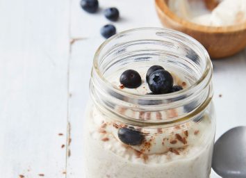 overnight cinnamon roll oats in open glass mason jar with blueberries on wooden tabletop with spoon