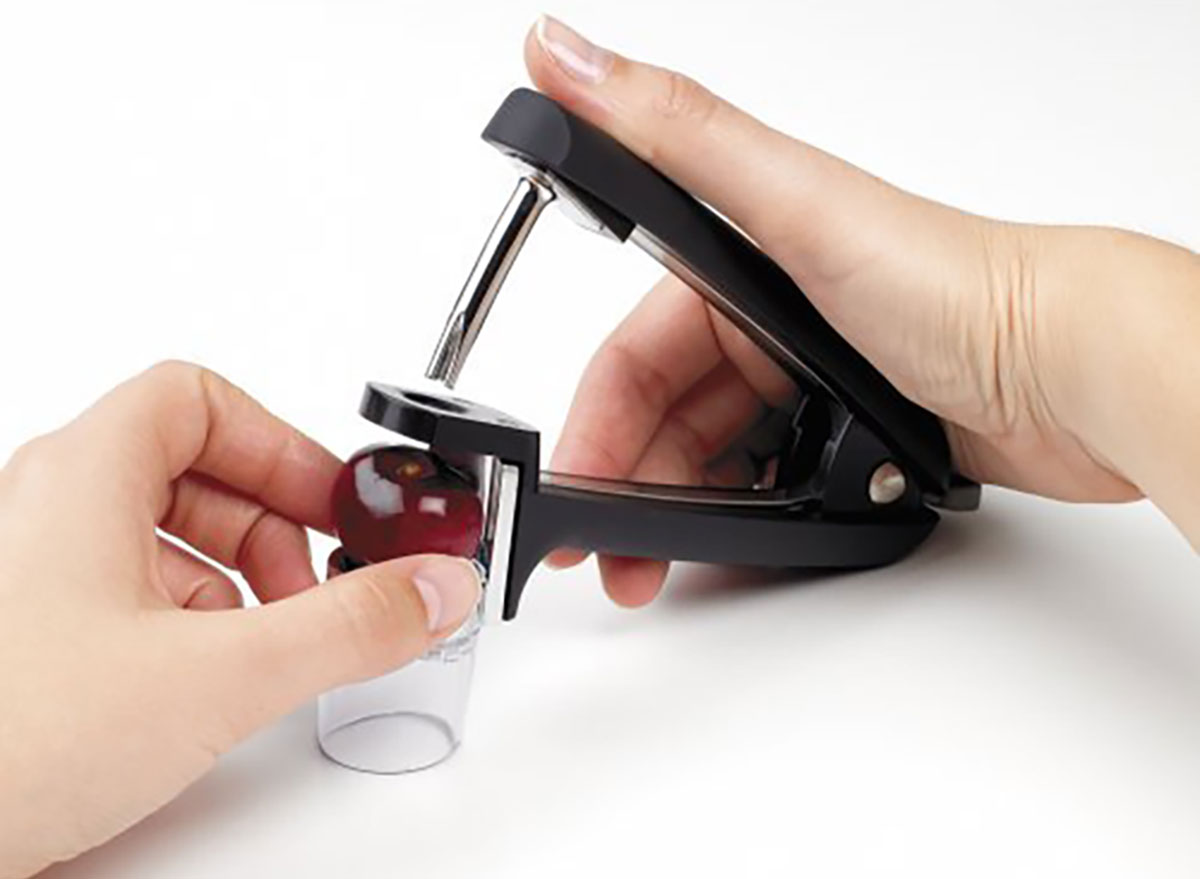 oxo olive cherry pitter with person's hands pitting a cherry