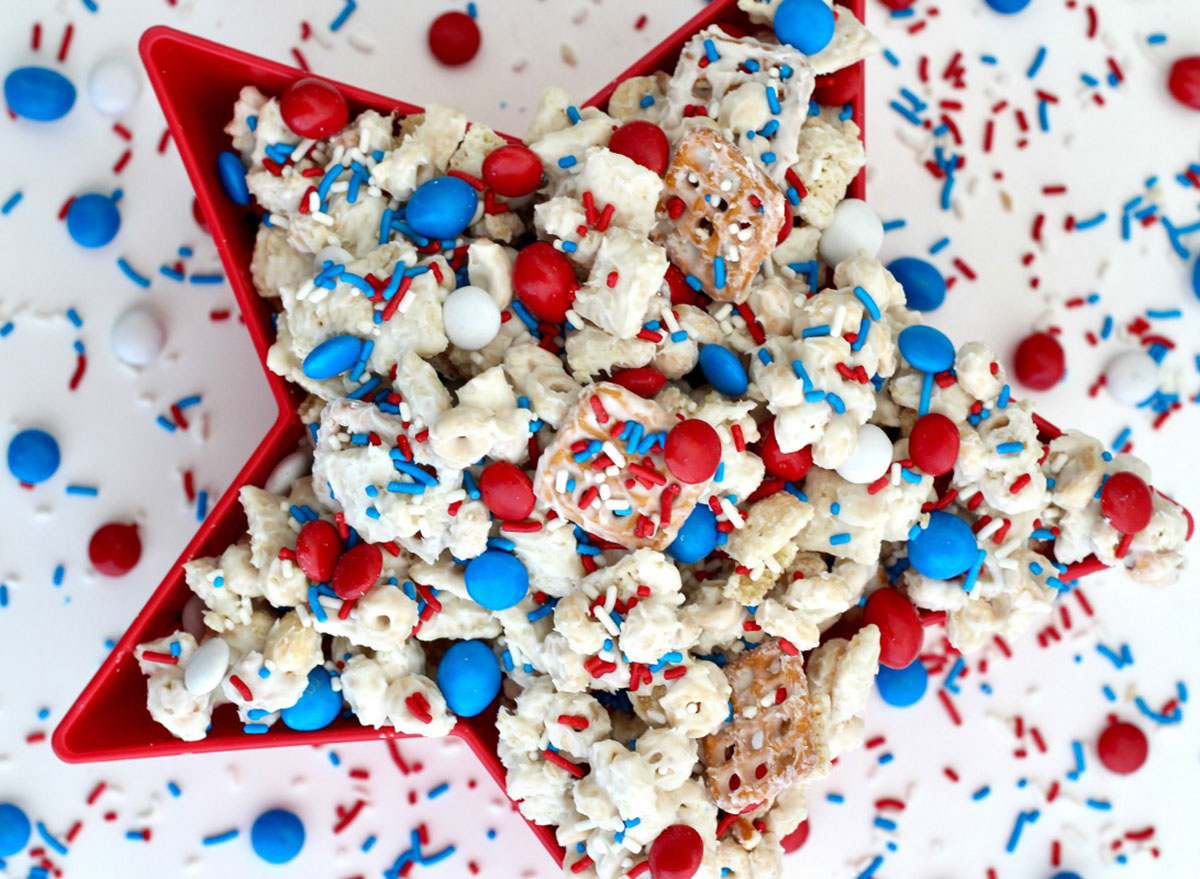 chex mix with red white and blue m&ms and sprinkles in red star bowl with sprinkles on white background