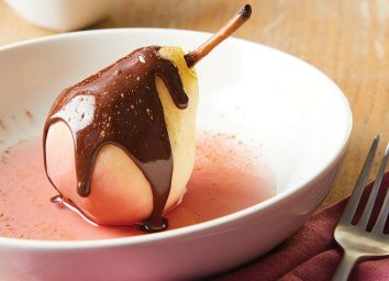poached pear with spiced chocolate sauce in white bowl with fork
