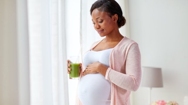 pregnant african american woman drinking green vegetable juice or smoothie at home