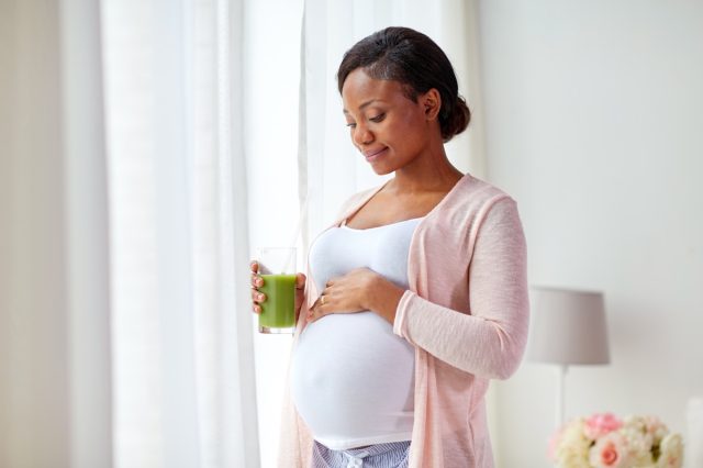 pregnant african american woman drinking green vegetable juice or smoothie at home