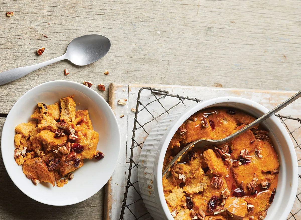 two bowls of pumpkin bread pudding with spoons on wire rack and wooden background