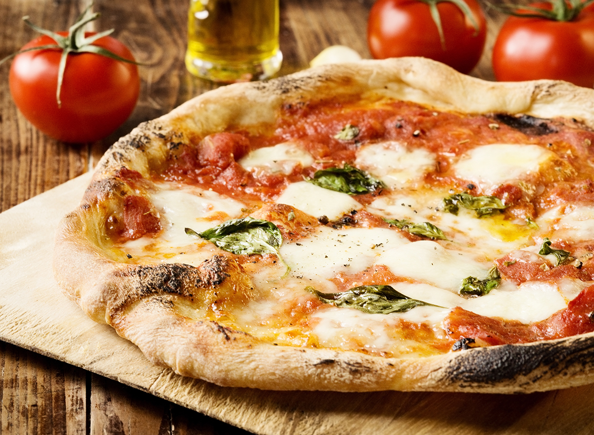 neapolitan style pizza on a cutting board with tomatoes and olive oil