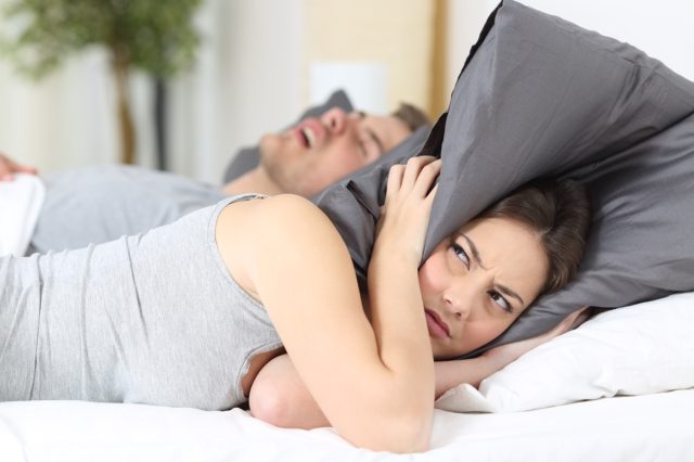 Mann schnarcht, während seine Frau die Ohren mit dem Kissen bedeckt