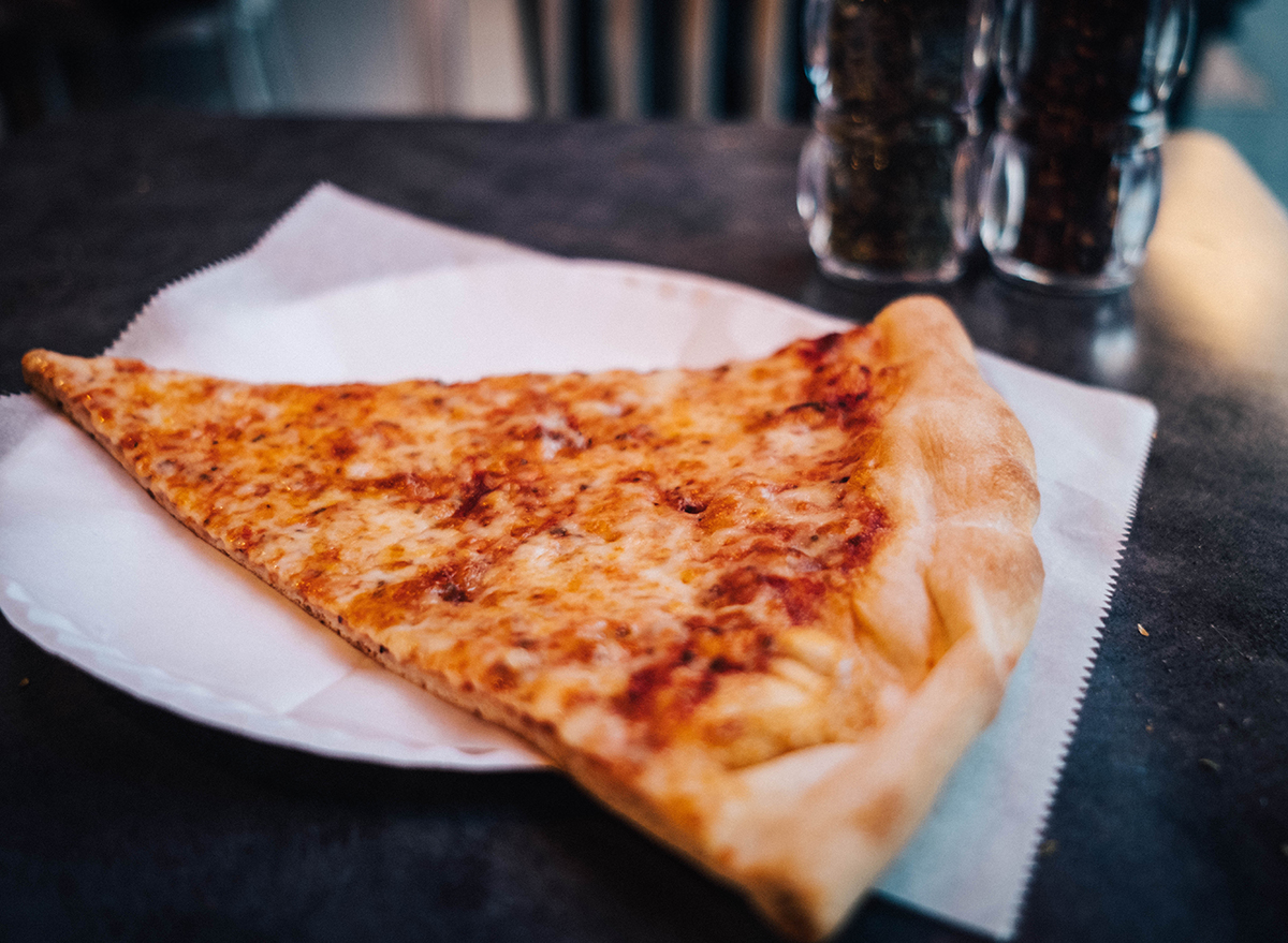 slice of new york style pizza on a paper plate and counter in the city