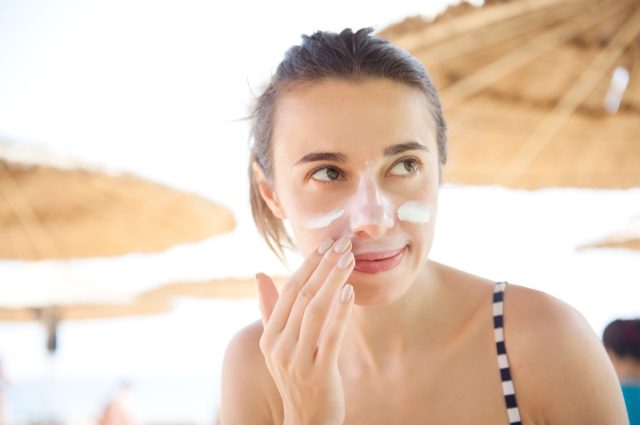 la donna spalma la crema solare per il viso in spiaggia per protezione