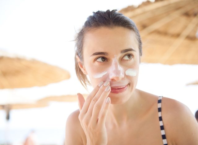 woman smears face sunscreen at the beach for protection