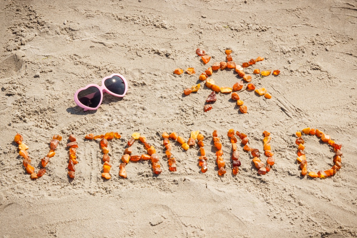Sunglasses, inscription vitamin D and shape of sun made of amber stones at beach, concept of vacation time and prevention of vitamin D deficiency