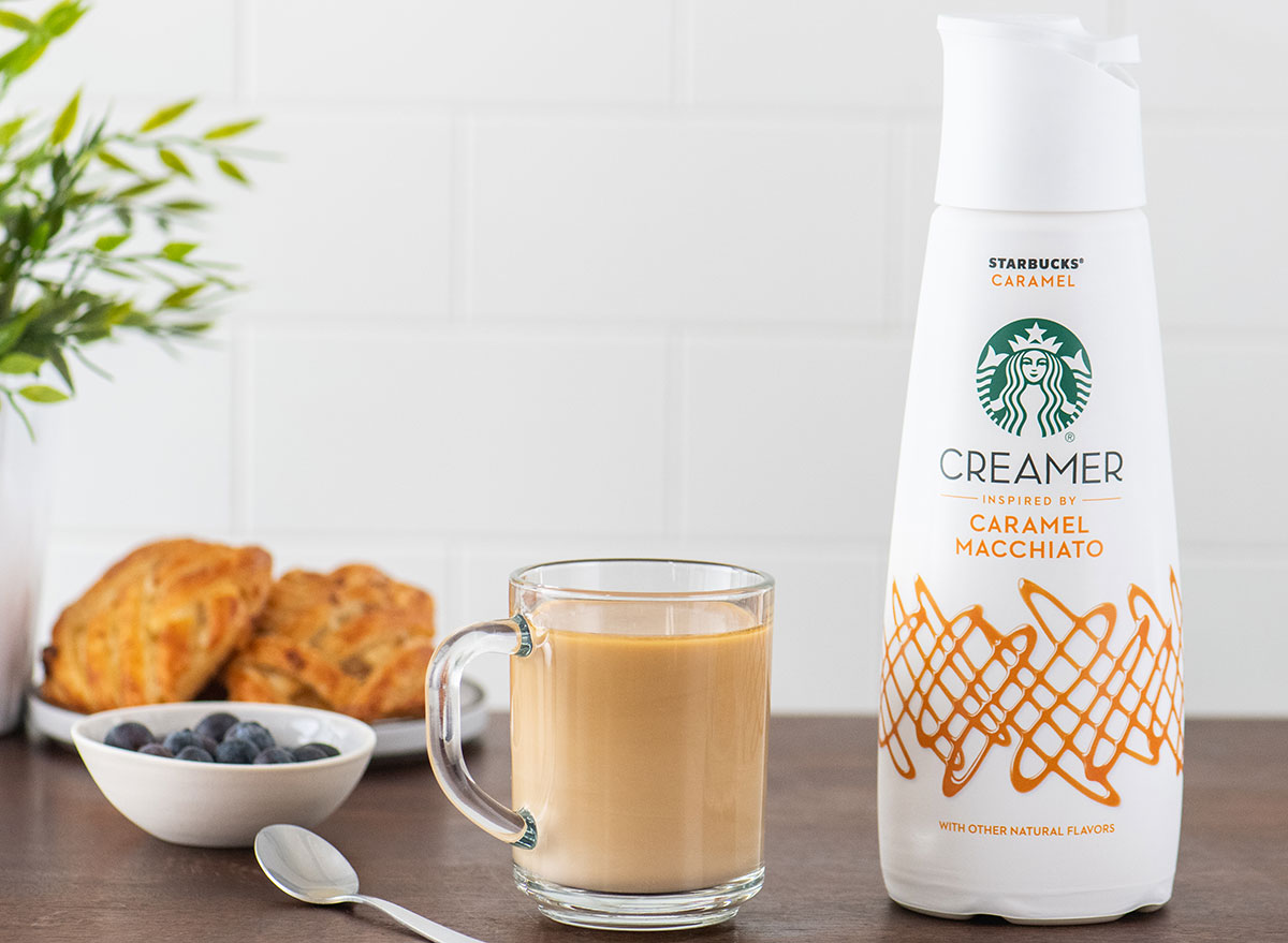 container of starbucks caramel macchiato coffee creamer with glass cup of coffee and scones on table