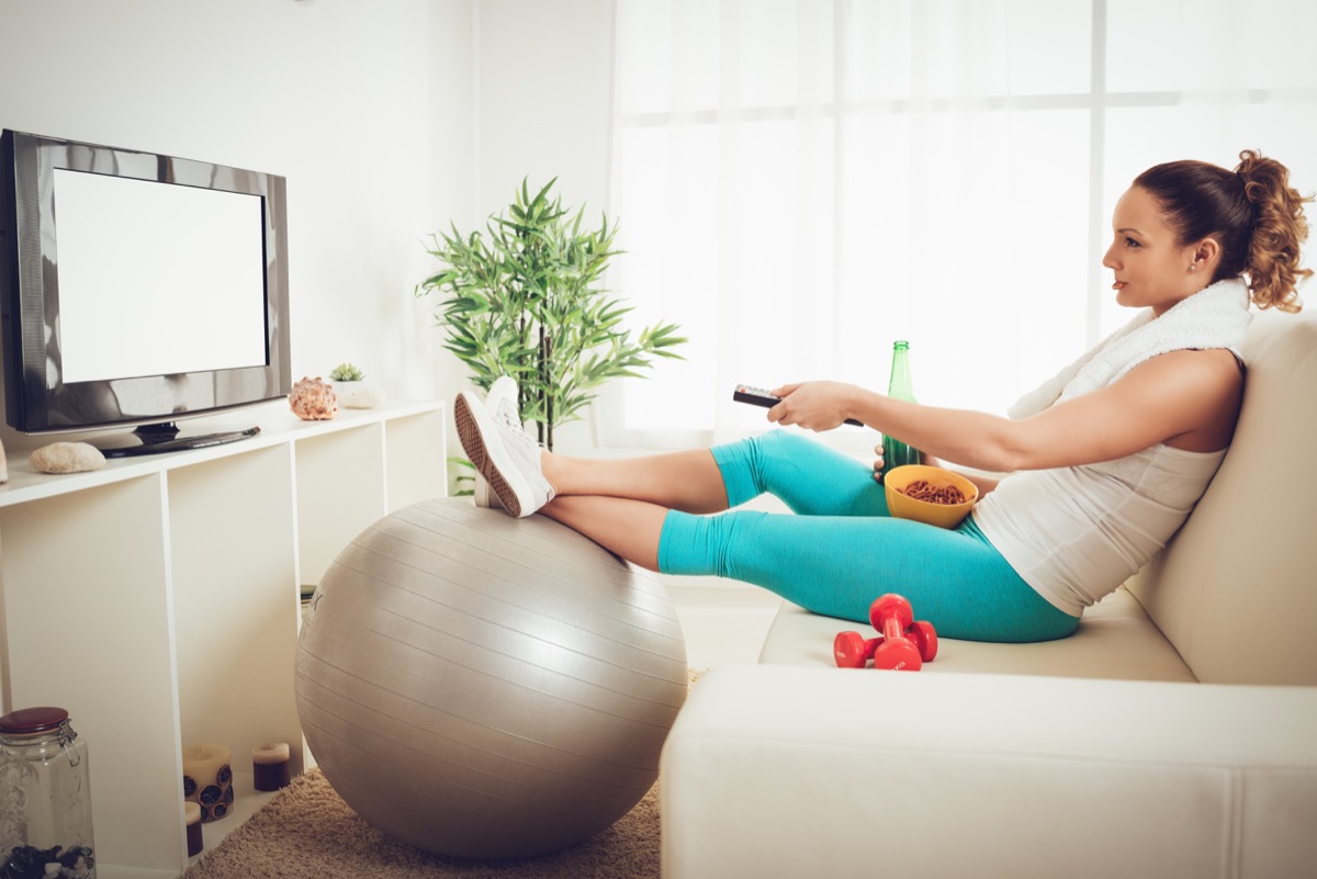 young woman in sport clothing sitting front of the TV and doesn't wont to exercise