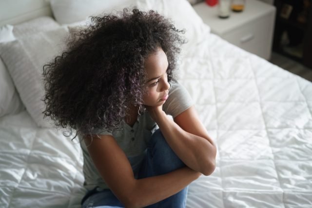 Jeune femme latine solitaire assise sur le lit.  Fille hispanique déprimée à la maison, regardant loin avec une expression triste