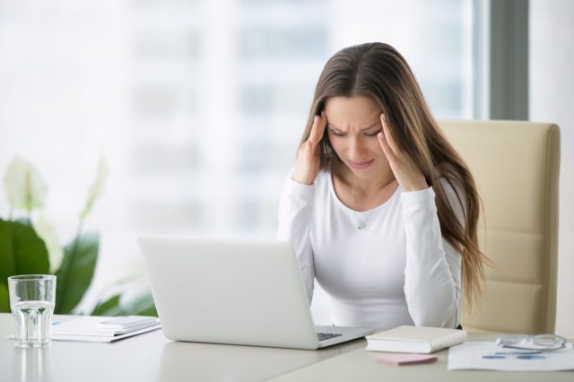Young frustrated woman working at office desk in front of laptop