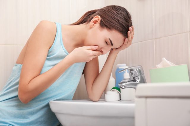 Young woman vomiting near sink in bathroom