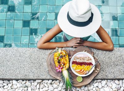 woman poolside at resort with smoothie bowl fresh fruit