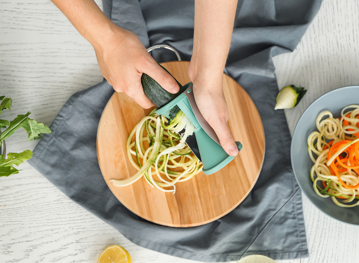Woman spiralizing zucchini on a counter with other spiralized vegetables shutterstock