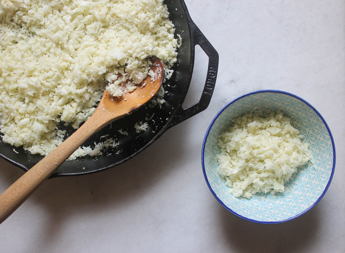 cauliflower rice in a skillet scooped into a blue bowl on a marble counter