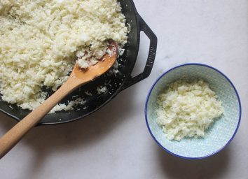 cauliflower rice in a skillet scooped into a blue bowl on a marble counter