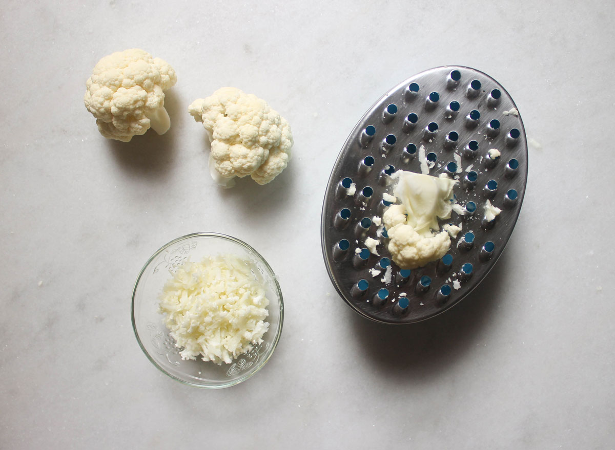 cauliflower florets being grated into rice on a marble counter