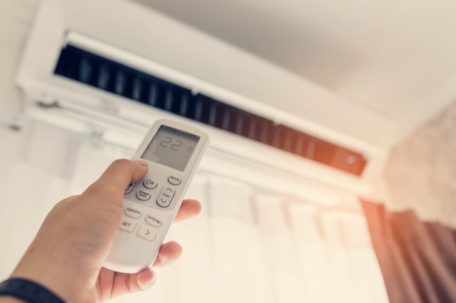 Air conditioner in the room with woman operating the remote control