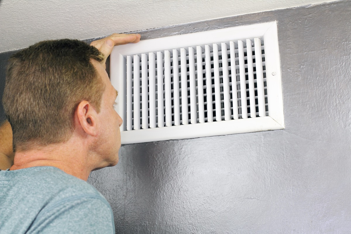 man examining an outflow air vent grid and duct to see if it needs cleaning