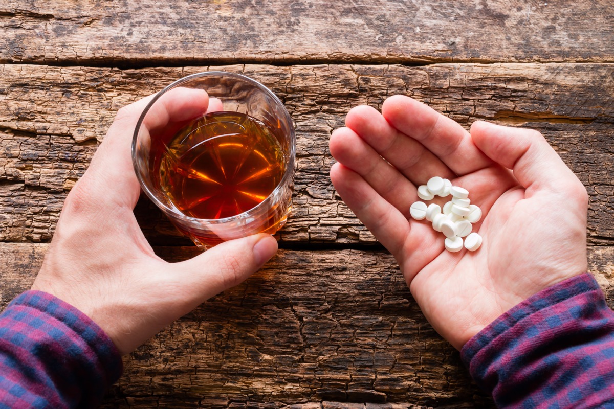 man holding a glass of alcohol and a handful of pills
