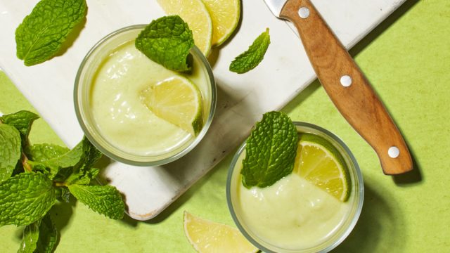 avocado lime smoothie on a white cutting board with limes and a knife on a green table